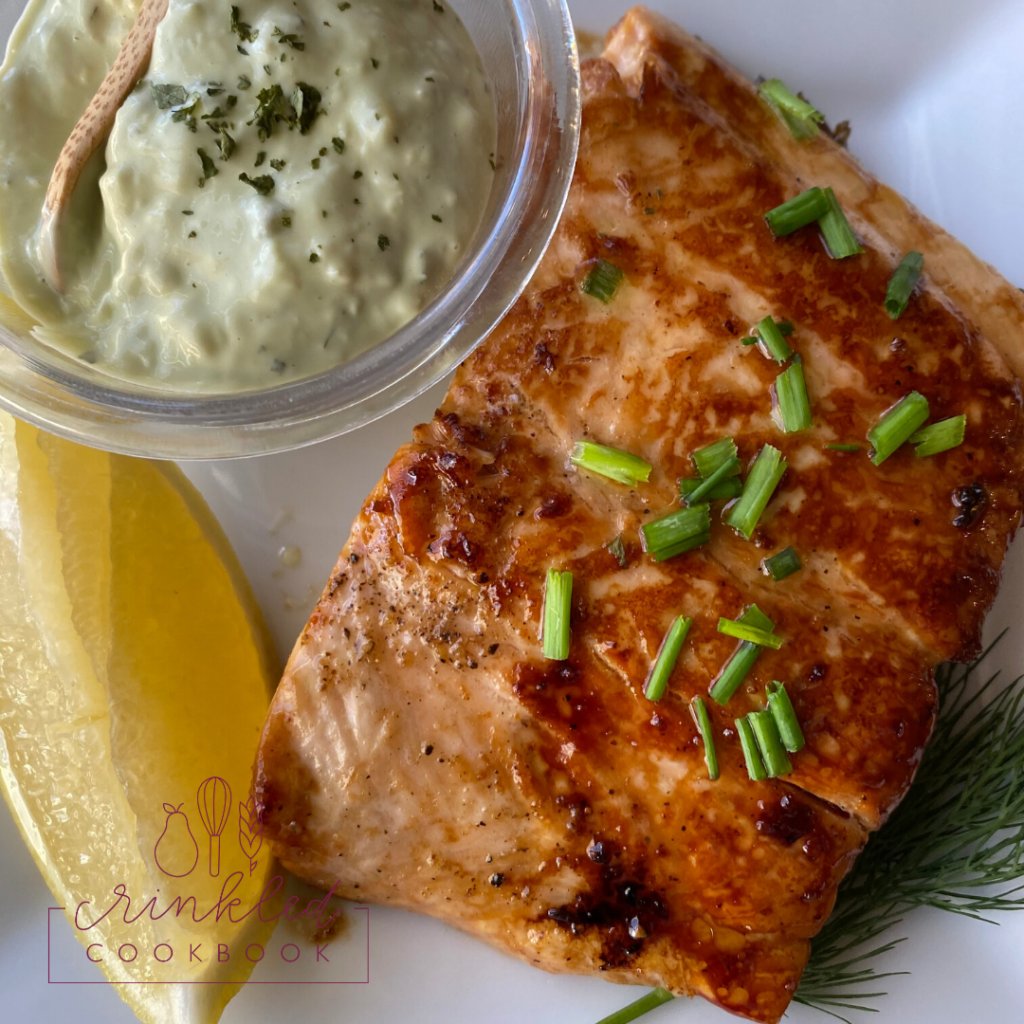 Skillet-glazed salmon on a plate with lemon and a dish of tarter sauce.