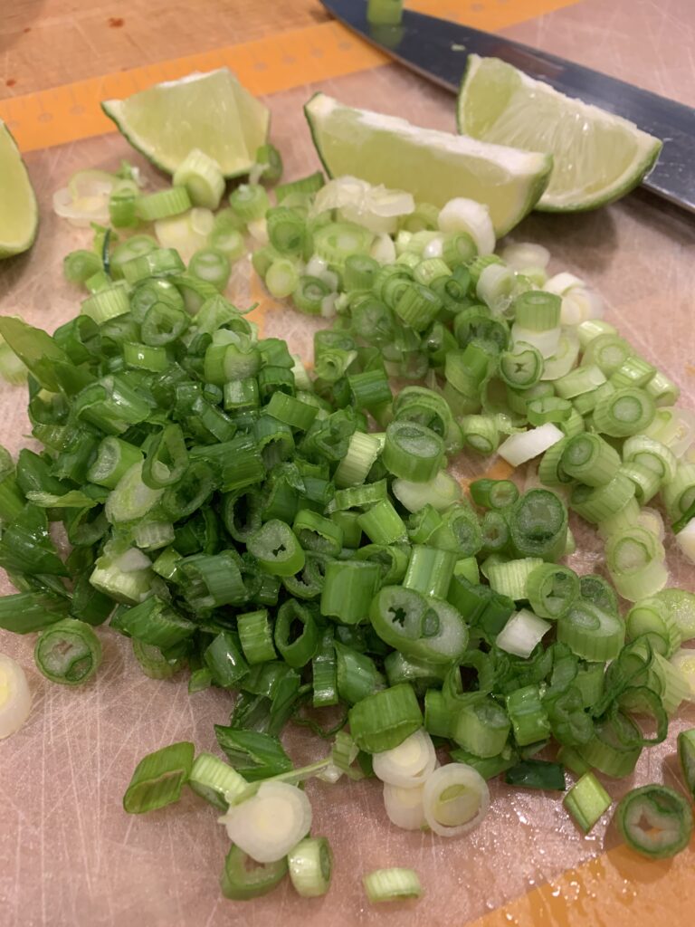 Chopped green onions and lime wedges on a cutting mat. 