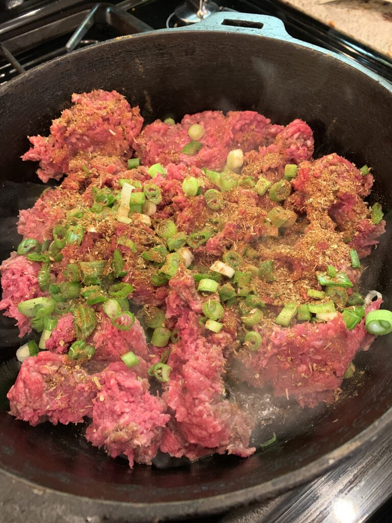 Ground beef and green onions in a skillet. 