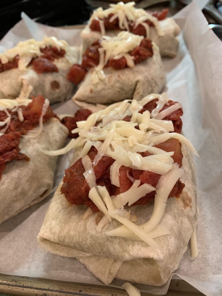 Burritos covered with tomato sauce and cheese on a baking dish. 