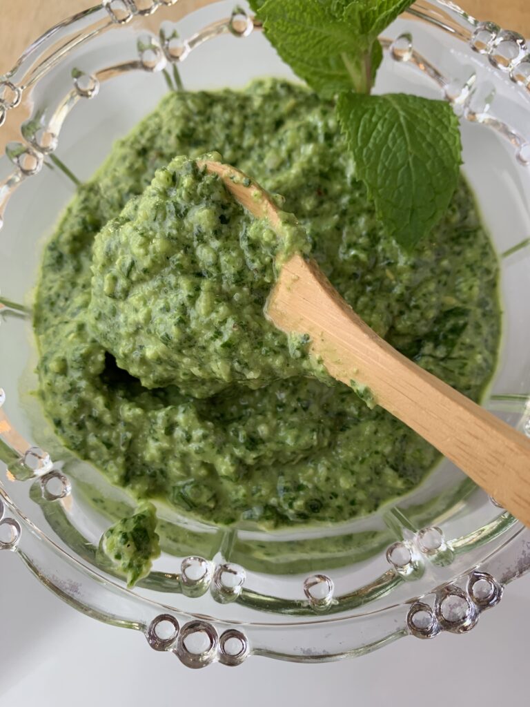 Pesto sauce in spoon over a bowl of pesto