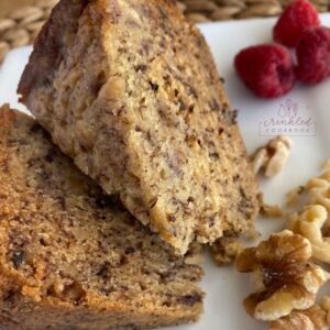 Banana bread sliced into wedges with raspberries in the background.