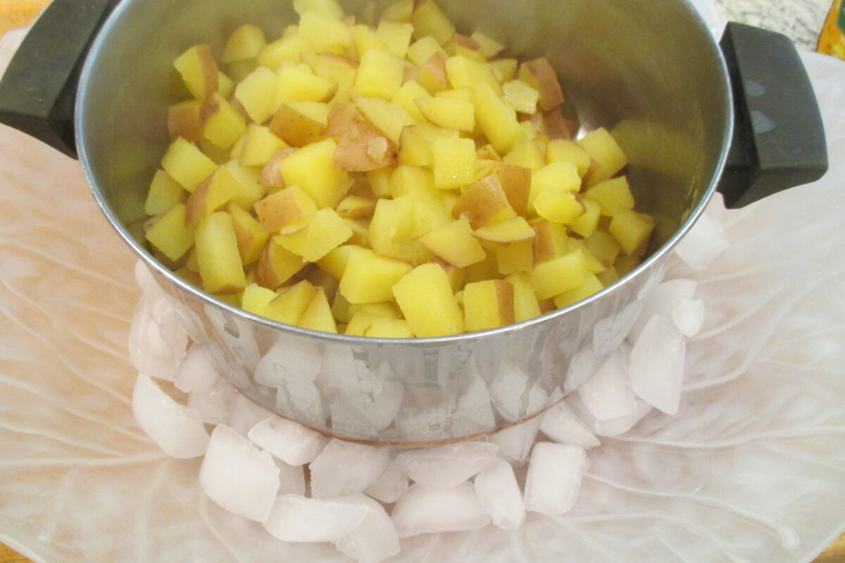 Diced potatoes in a pan setting on top of ice cubes. 