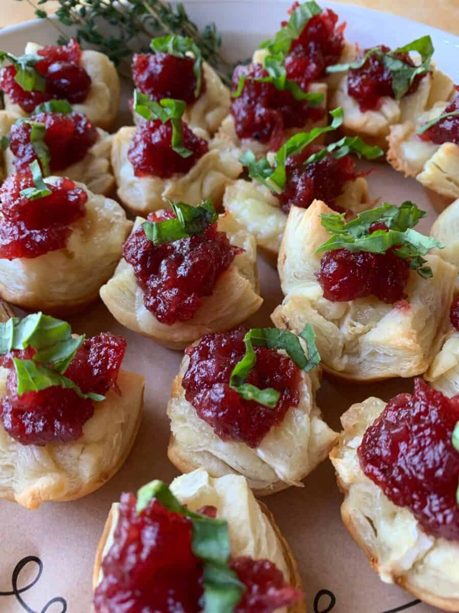 Cranberry brie bites with basil on top, spread out on a dish