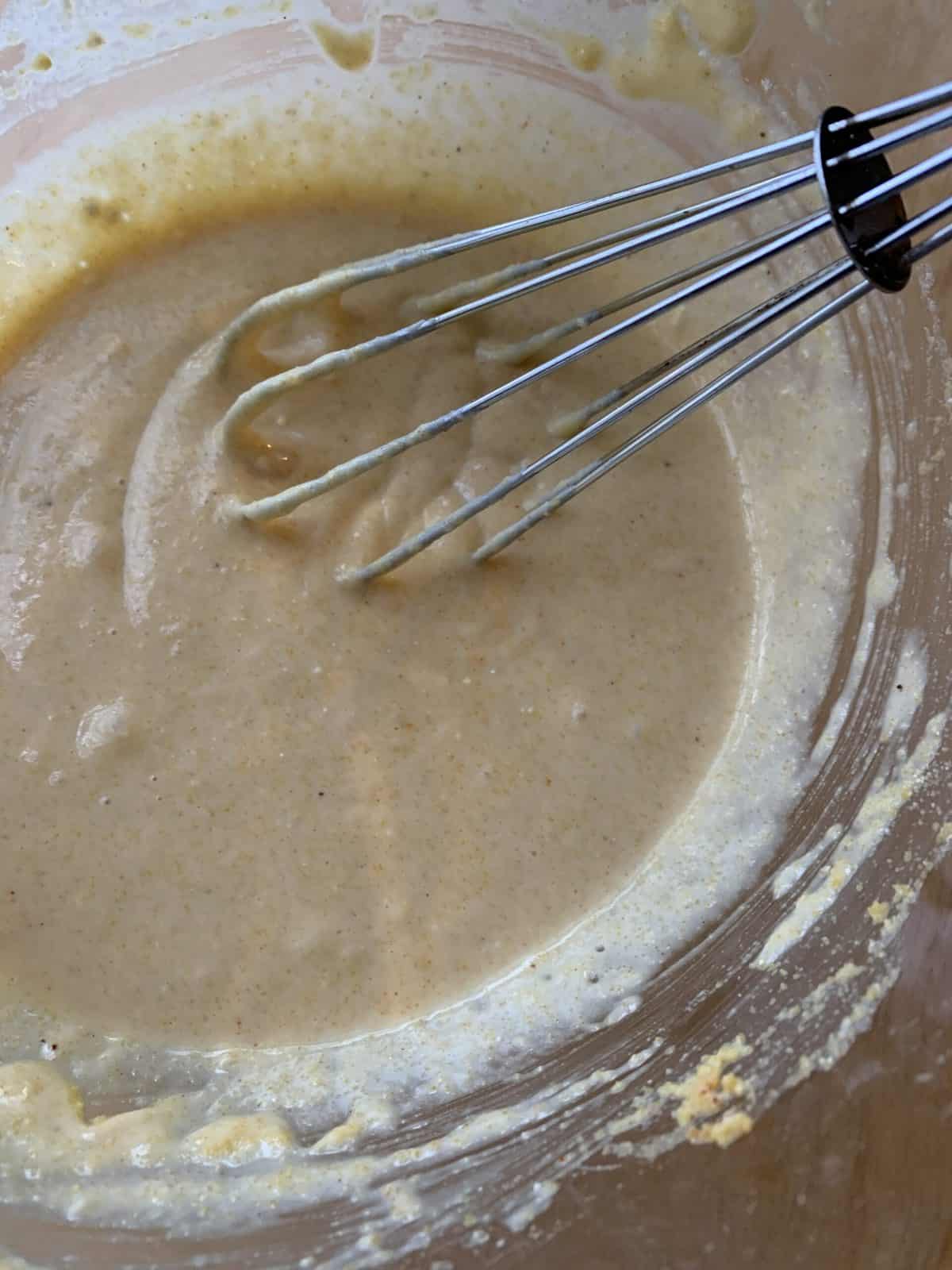 Corn dog nugget corn meal batter in a small bowl with a whisk. 