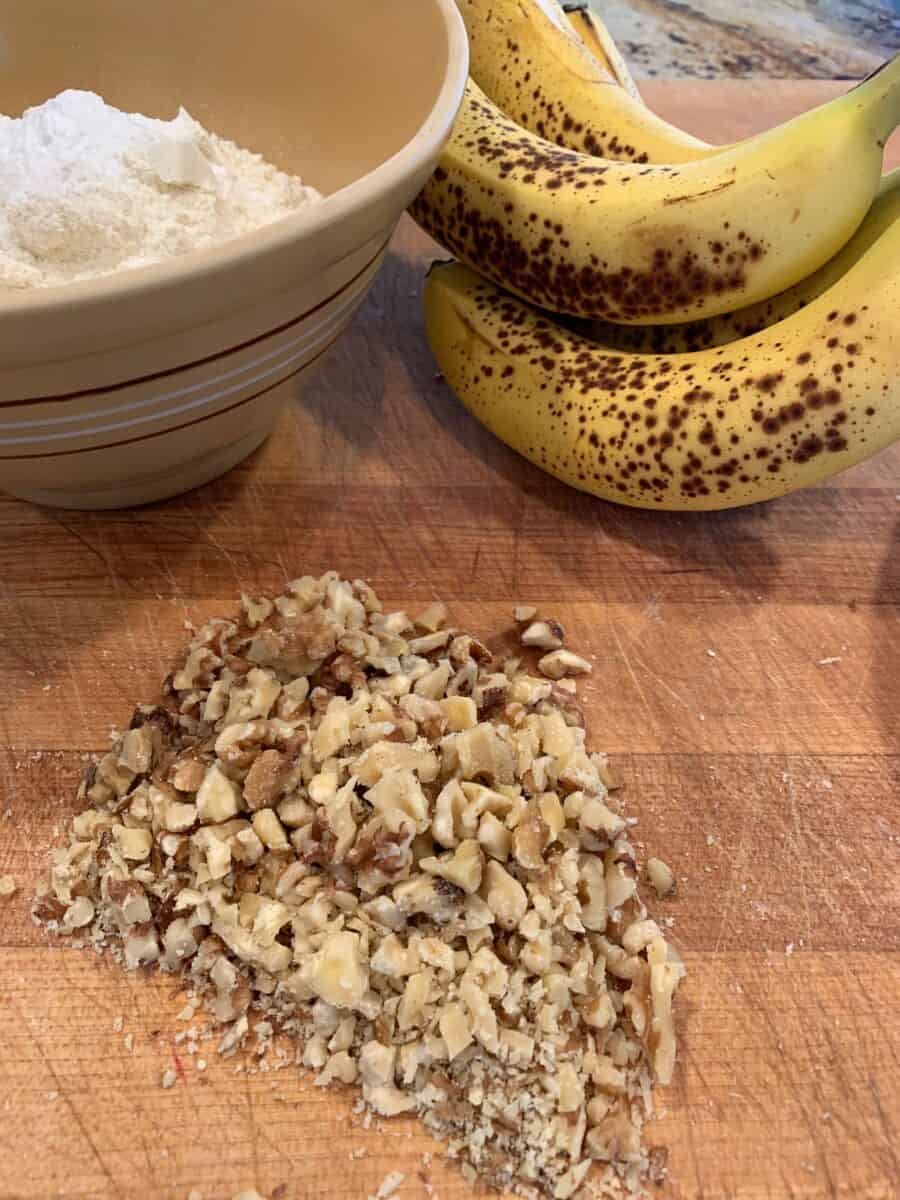 Chopped walnuts, ripe bananas and a bowl on a cutting board.