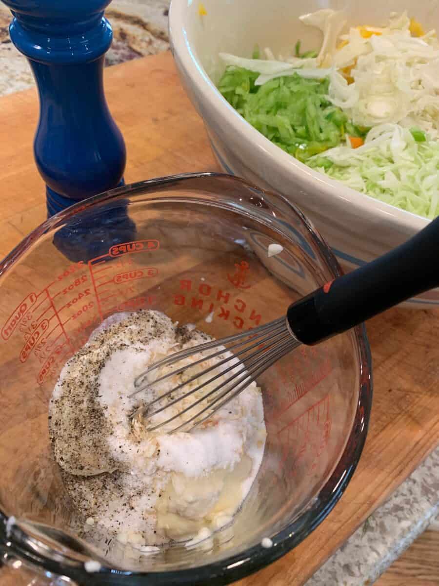 Cole slaw dressing ingredients in a glass measuring cup with a wise.