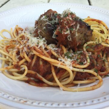 Meatballs on top spaghetti and sauce, with cheese garnish.