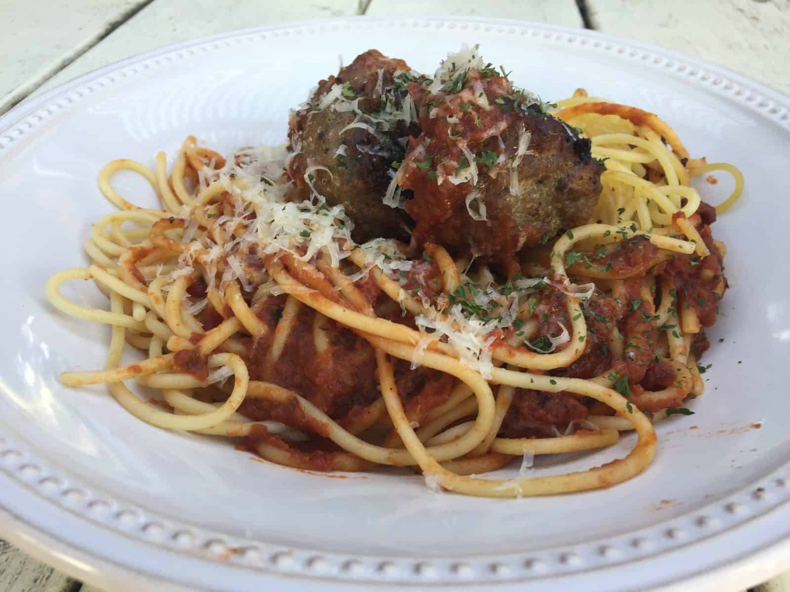 Meatballs on top spaghetti and sauce, with cheese garnish.