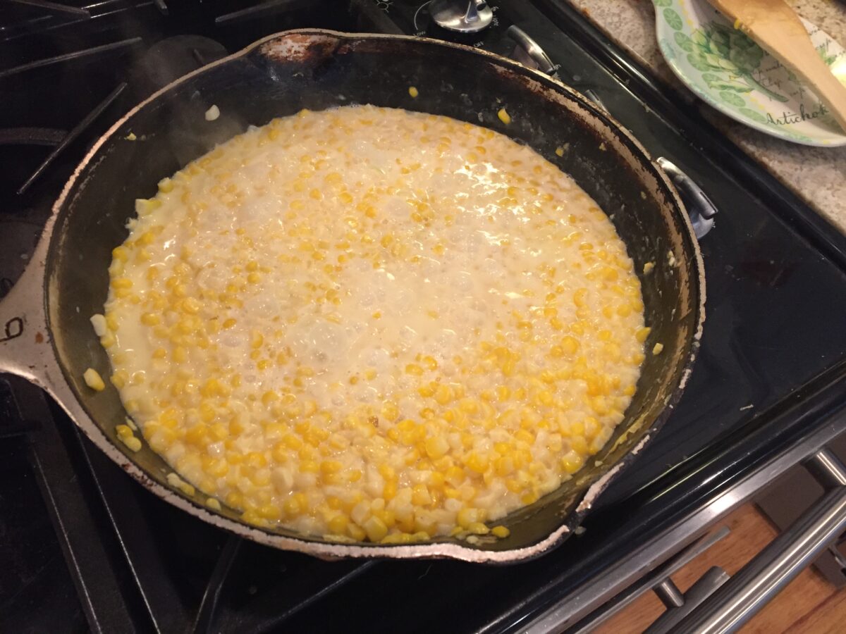 Corn simmering in a skillet on the stove.