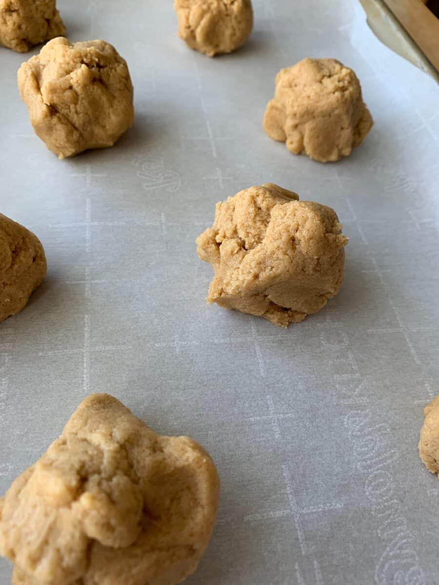 Raw peanut butter cookies on parchment paper on a baking sheet. 