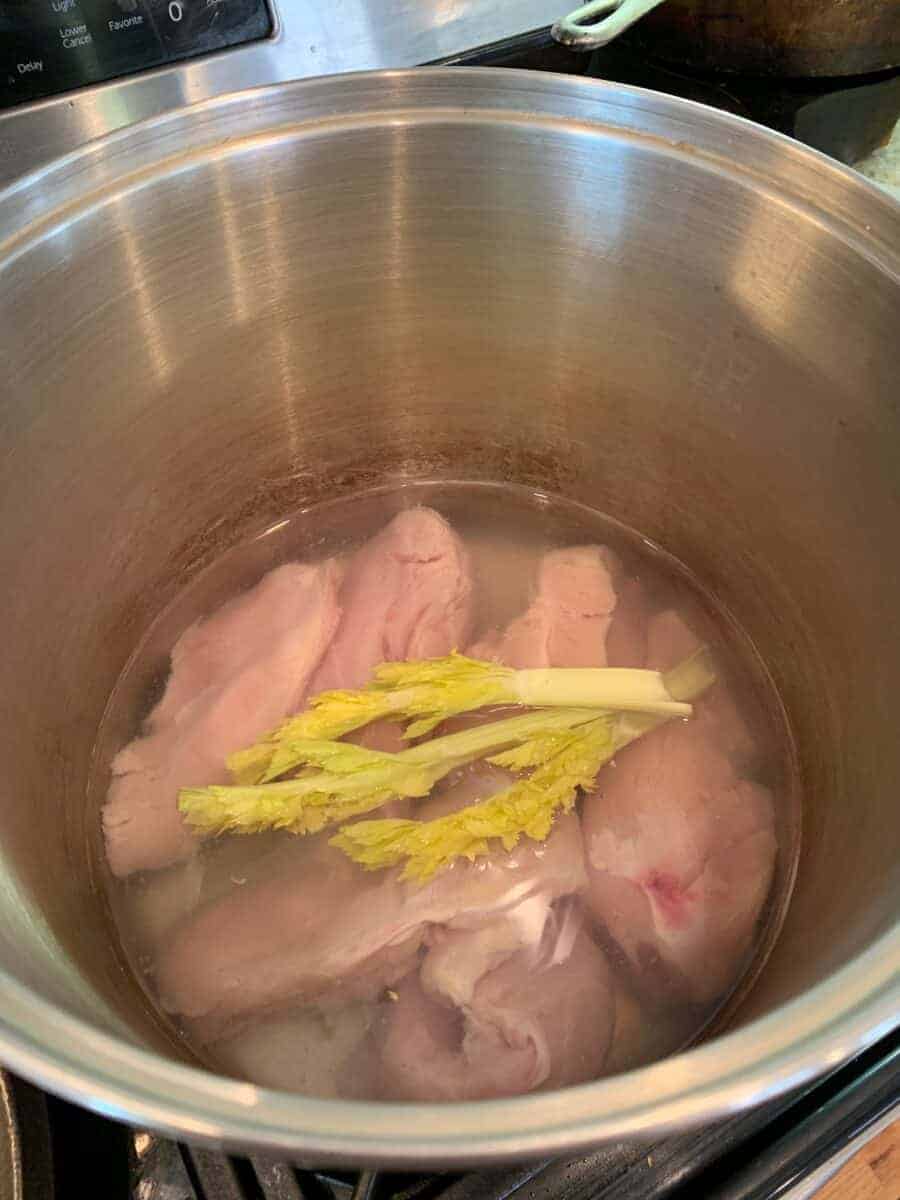 Raw chicken breasts and celery with water in a large stockpot.