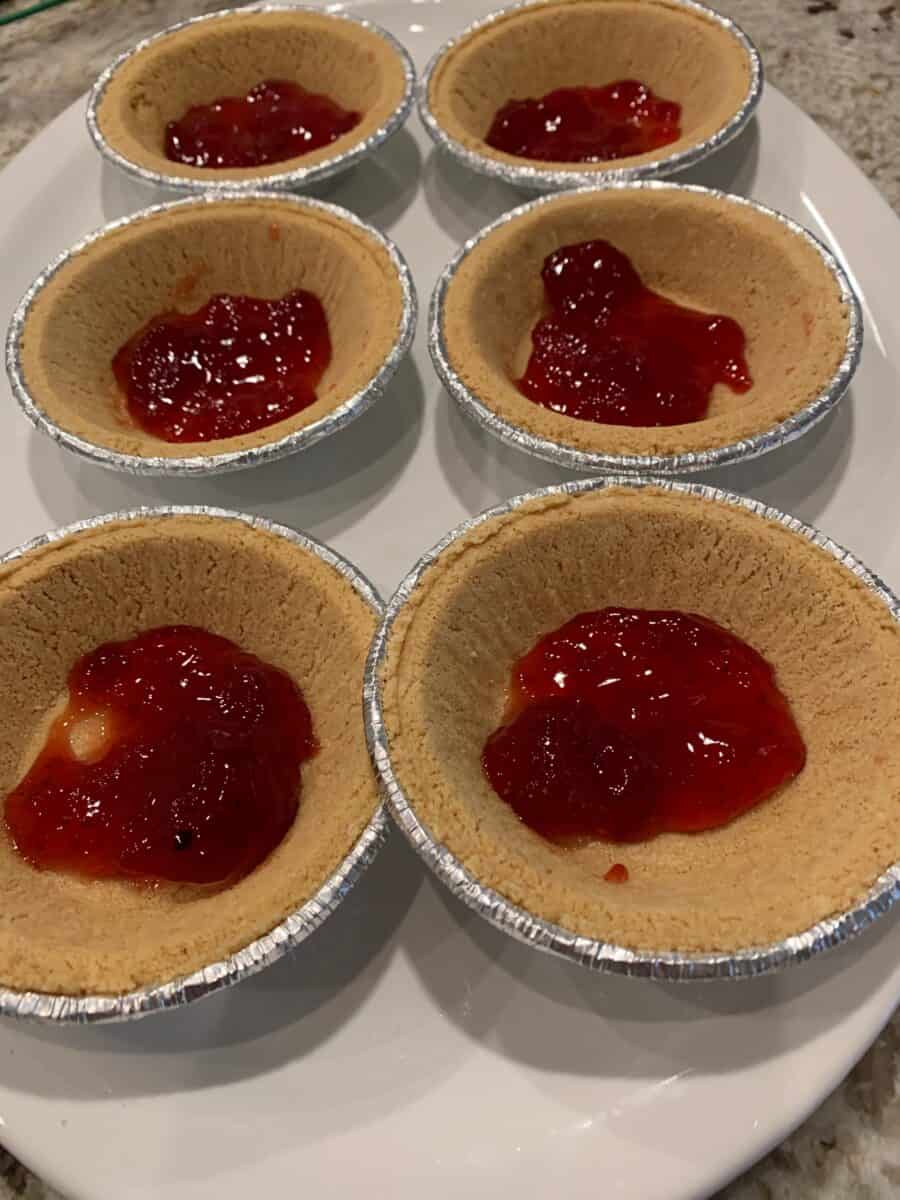 A layer of strawberry jam in the bottom of six mini pie crusts.