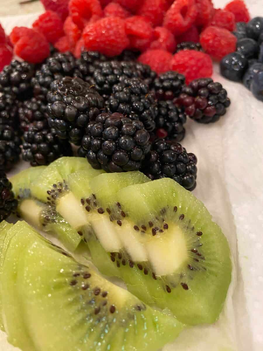 Sliced kiwi and mixed berries on a paper towel. 