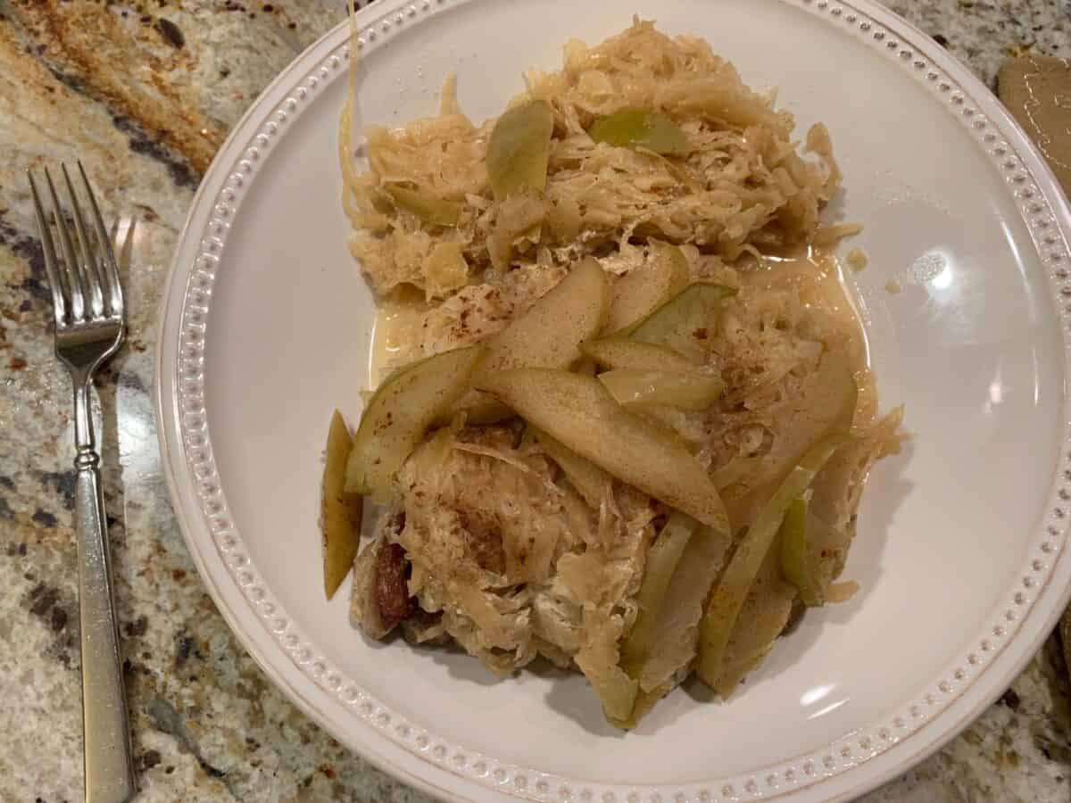 Diced, cooked apples and sauerkraut placed on top of cooked pork on a plate.