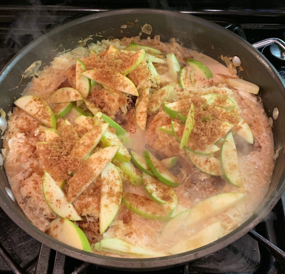 Pork chops, kraut and sliced apples in a large pan on the stove.