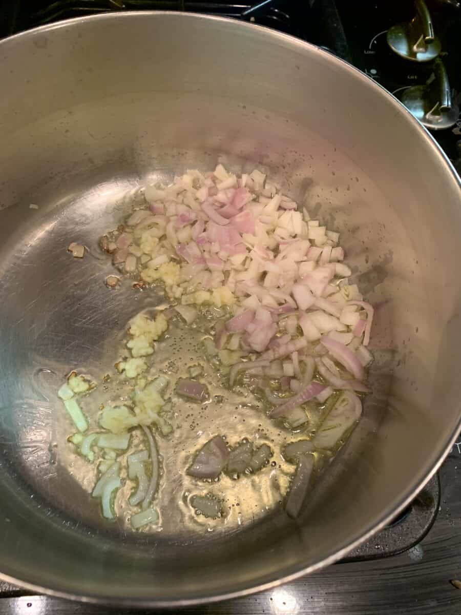 Shallots and garlic in a pan on the stove, simmering in olive oil.