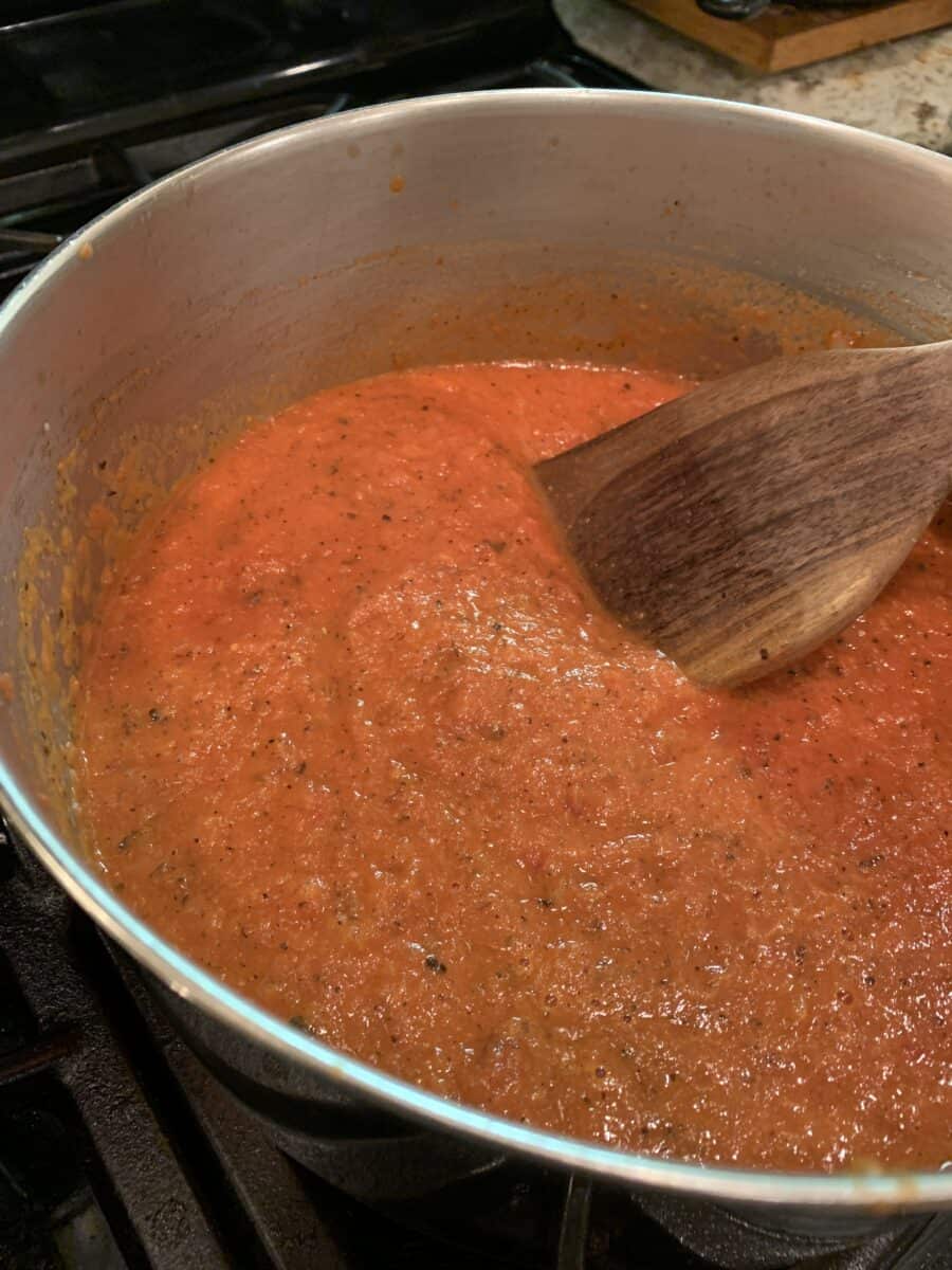 Tomato-cream sauce in a pan on the stove with a wooden spoon.