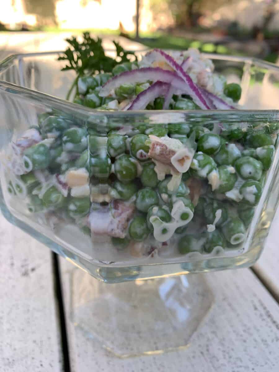 Pea salad in a glass serving bowl on an outdoor table. 