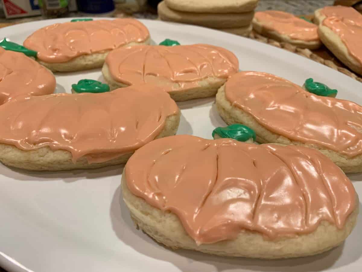 Frosted sugar cookies on a plate, with additional cookies stacked in the background.