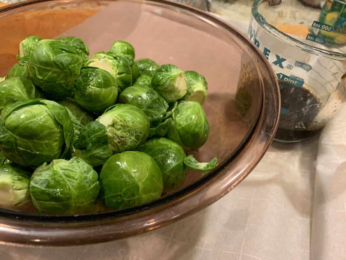 Veggies in a mixing bowl with vinegar and maple syrup mixture on the side. 