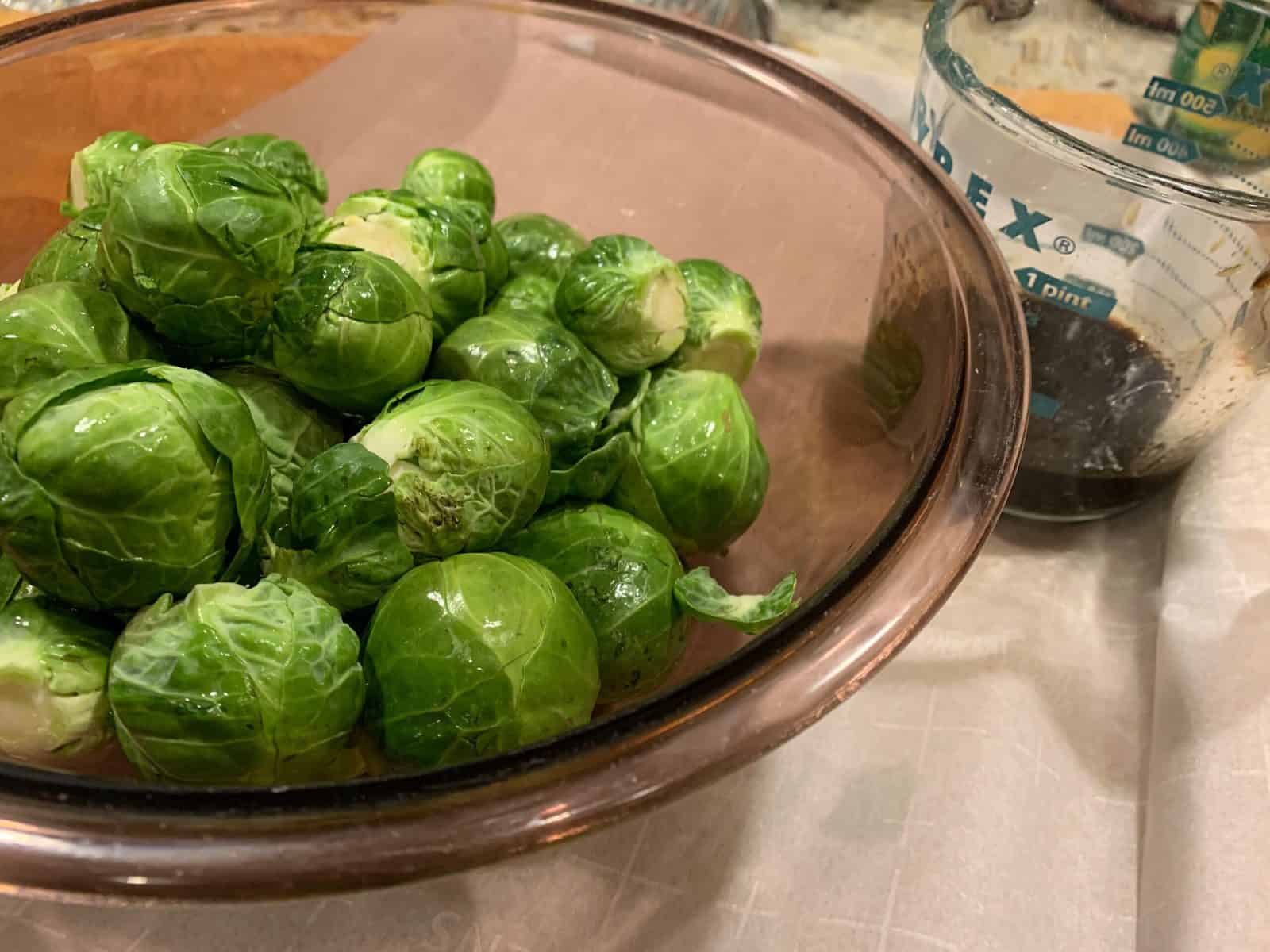 Veggies in a mixing bowl with vinegar and maple syrup mixture on the side.