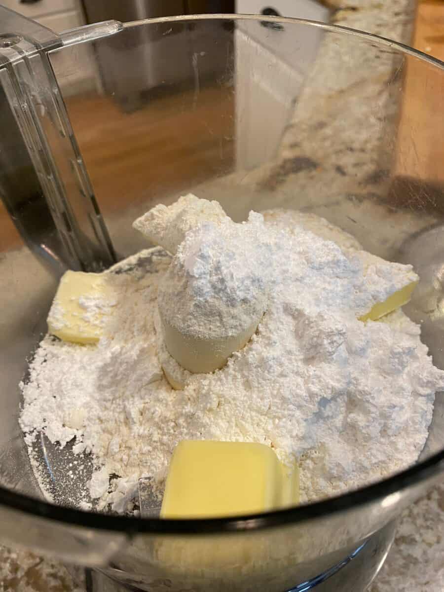 Butter with flour and powdered sugar in the bowl of a food processor.