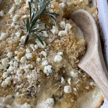Blue Cheese and Rosemary Scalloped Potatoes baked, with a wooden spoon in the dish for serving.