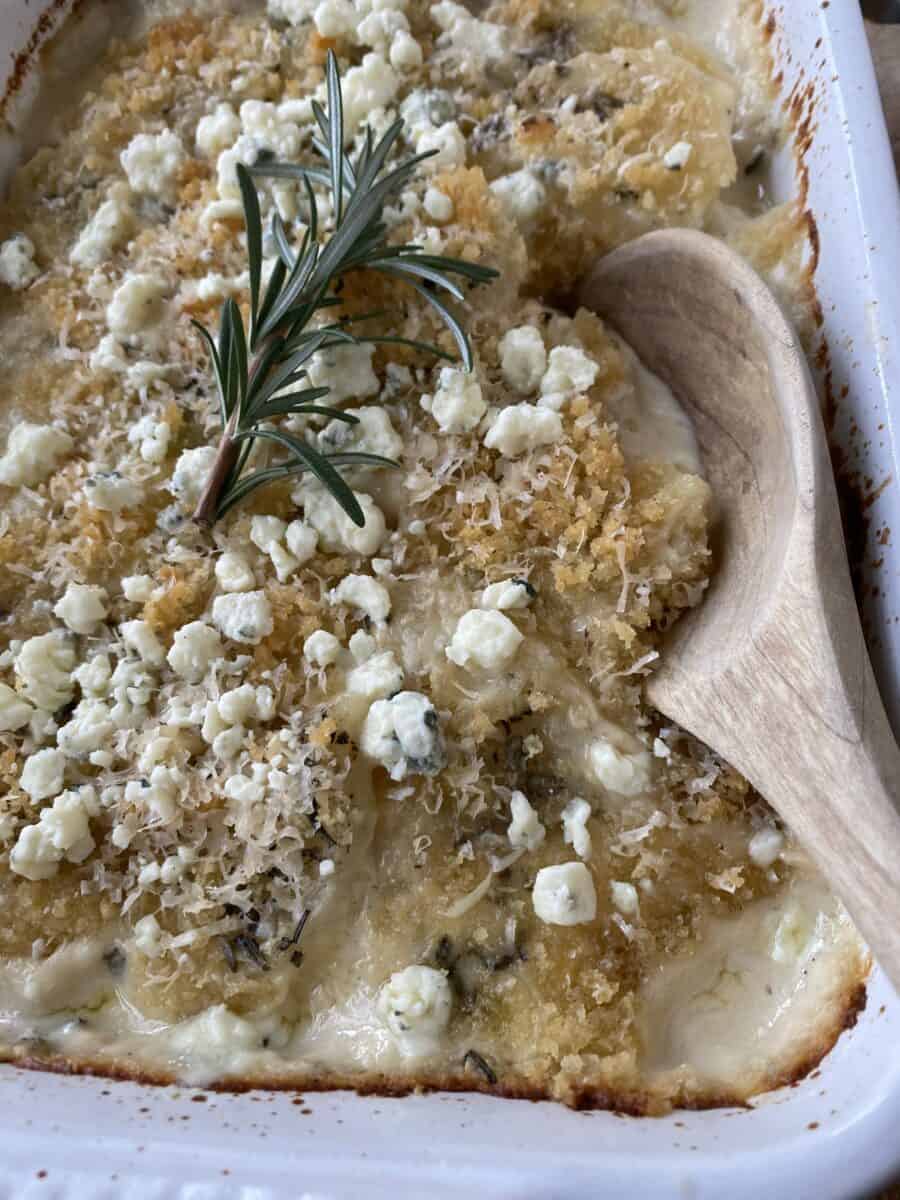 Blue Cheese and Rosemary Scalloped Potatoes baked, with a wooden spoon in the dish for serving.