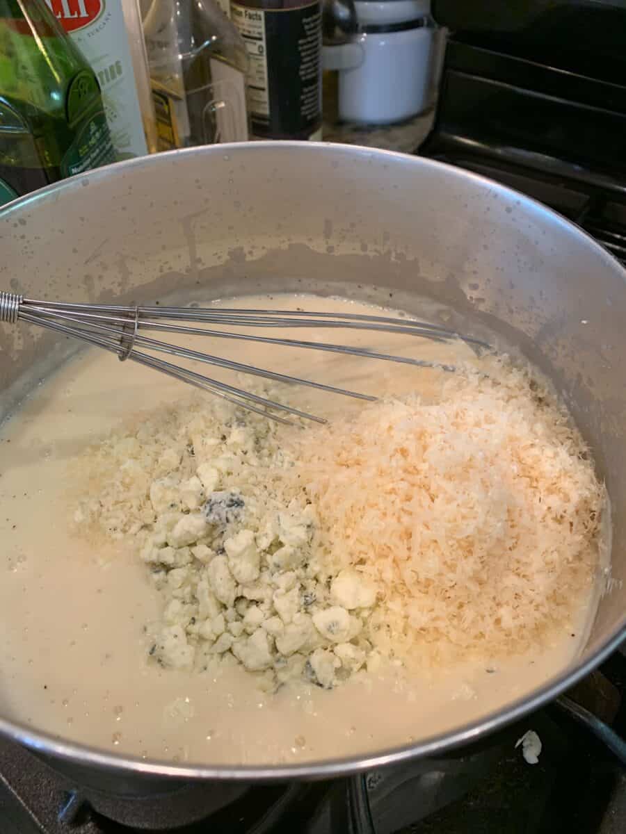 White sauce ingredients in a pan on the stove with a whisk. 