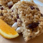 Rice Krispie treats stacked with a wedge of orange on the side.
