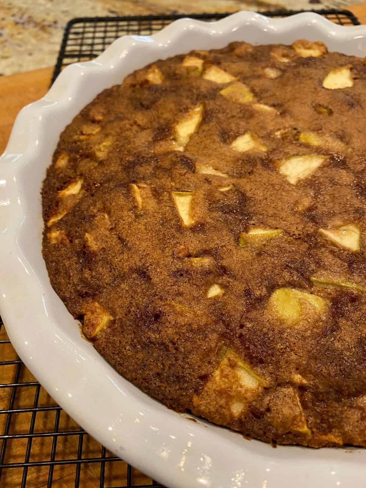 Apple cake in a pie dish on a cooling rack.