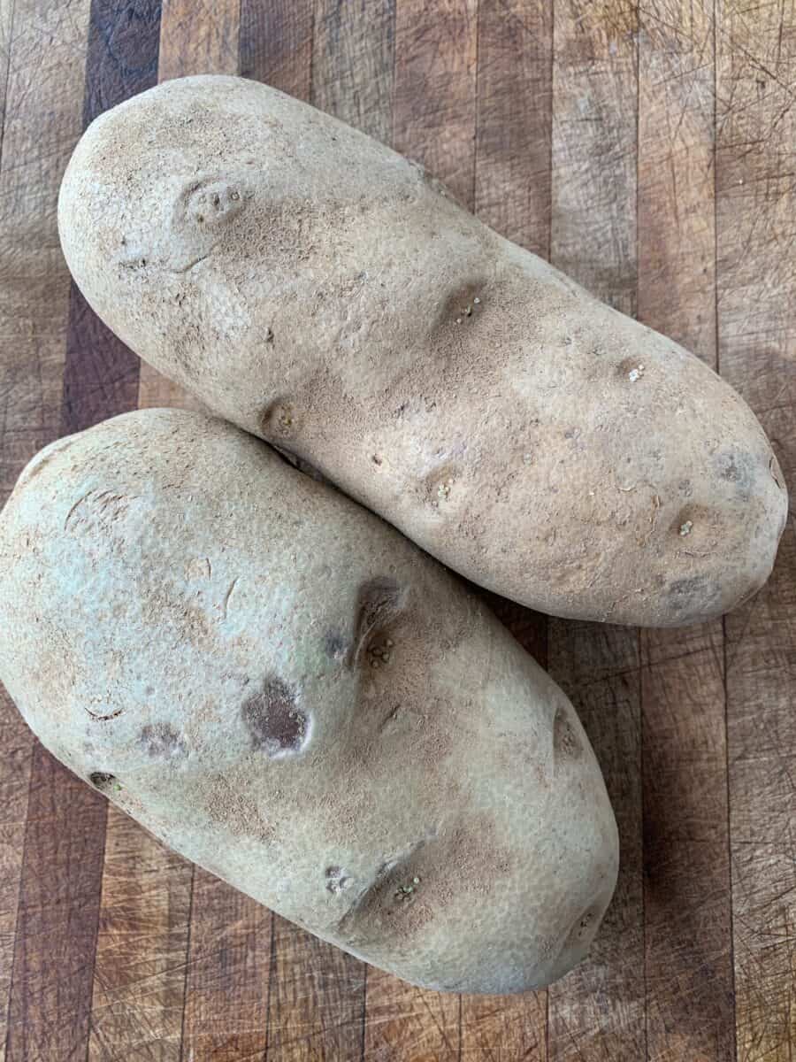 Two russet potatoes on a cutting board.