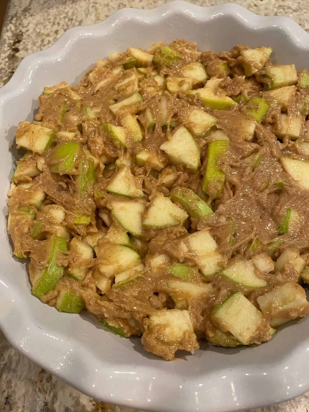 Unbaked apples with cake batter in a pie dish.