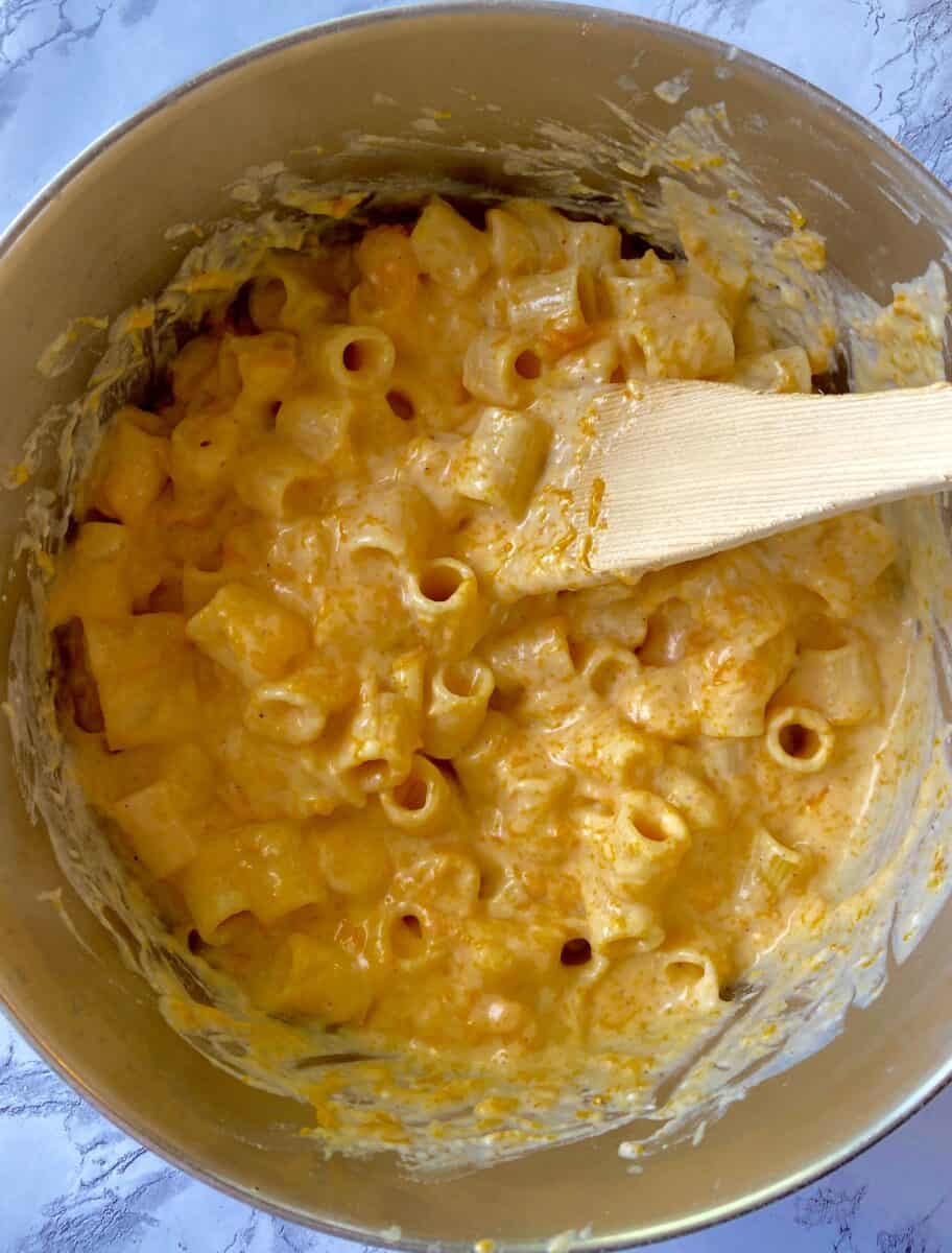 Pasta and cheese sauce in the pan, being stirred with a wooden spoon.