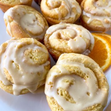 Orange sweet rolls arranged on a serving dish with a slice of orange.