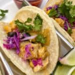 Small chicken tacos in a serving rack with lime, cilantro and salsa on the side.