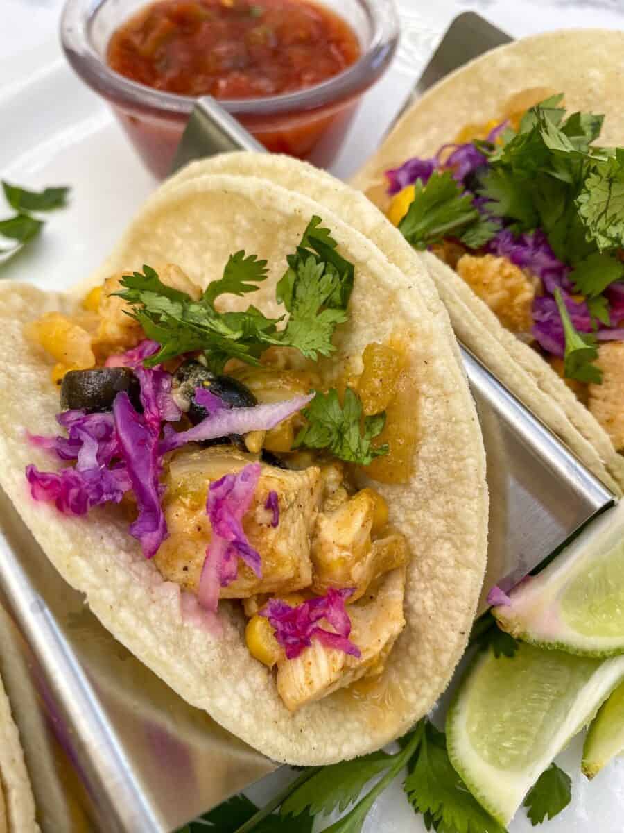 Small chicken tacos in a serving rack with lime, cilantro and salsa on the side.