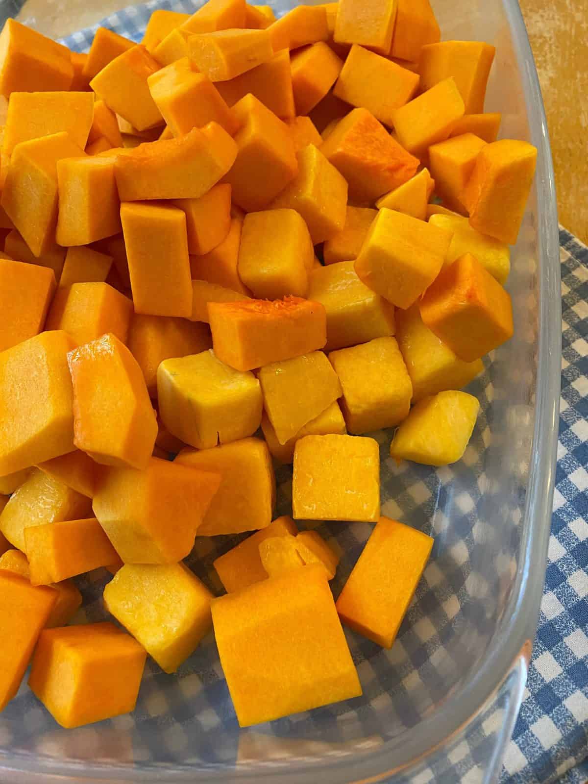 Diced butternut squash spread out in a glass baking dish on a placemat.