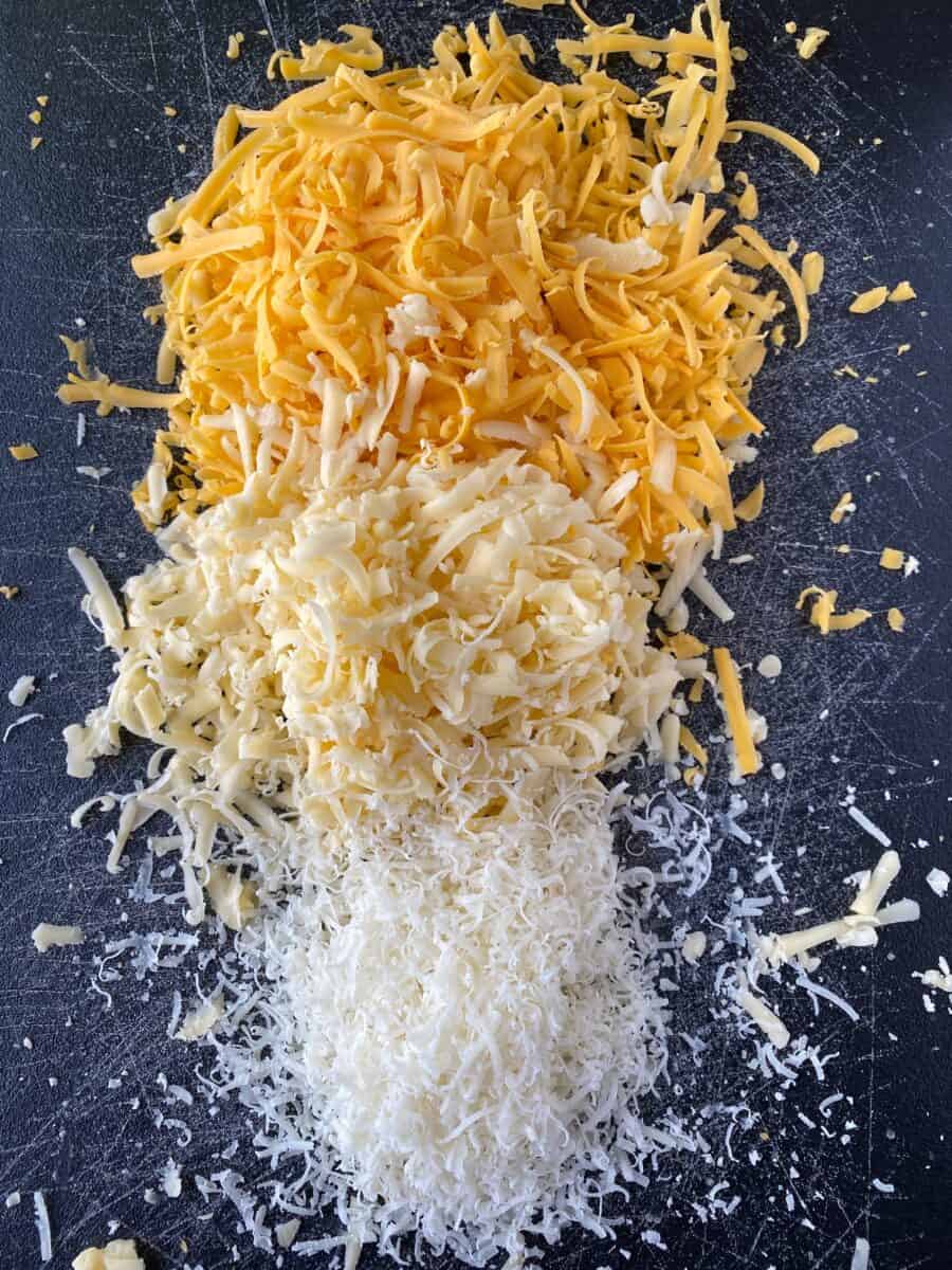 Three types of grated cheese mounded on a cutting board.