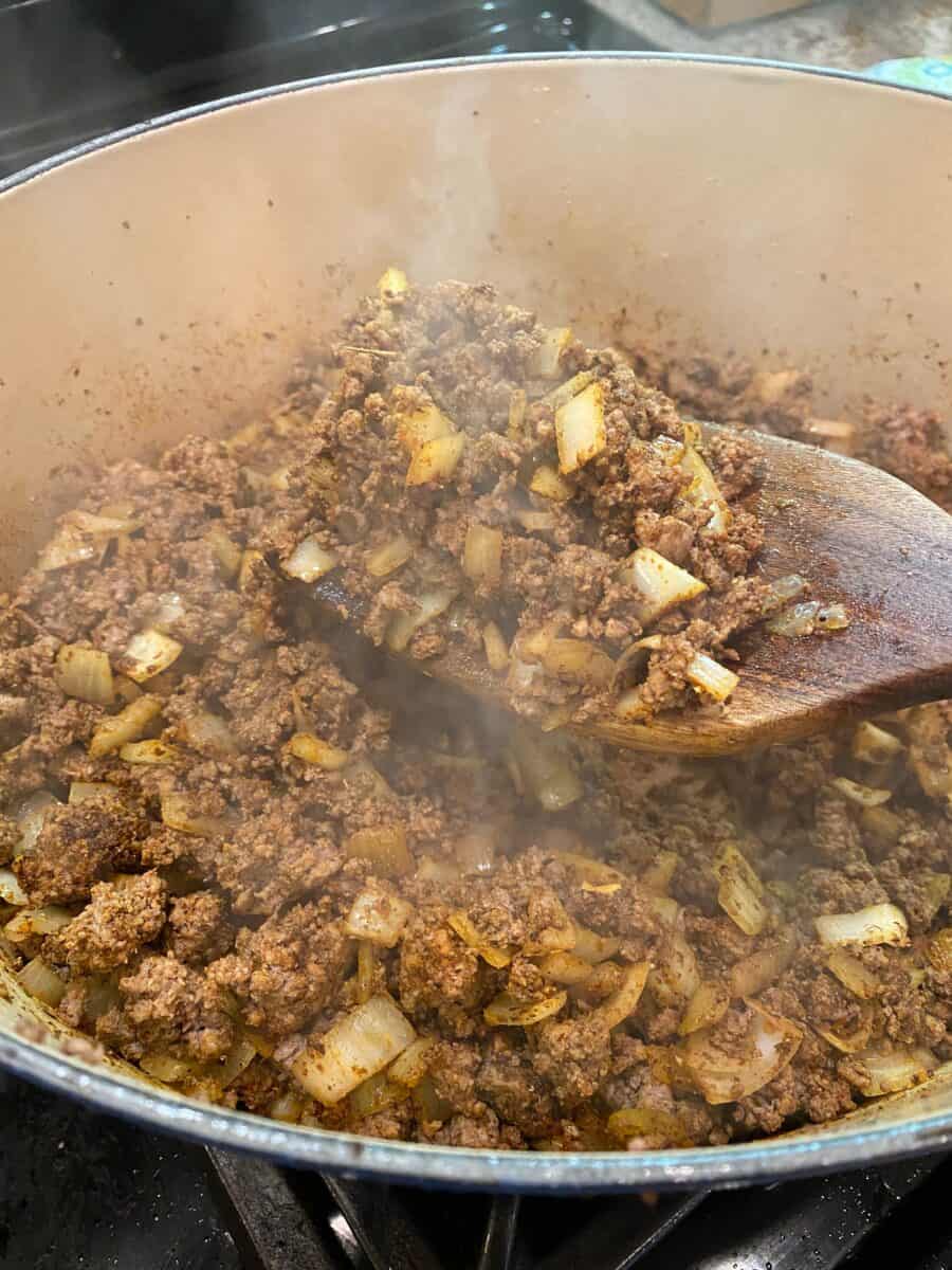 Chili meat and onions browned and steaming in a pot on the stove.