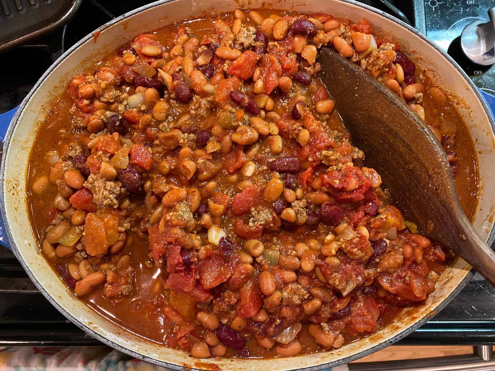 A large pot of chili on the stove with a wooden serving spoon.