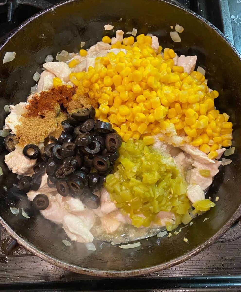 Olives, green chilies, corn, spices and chicken cooking in a cast iron skillet.