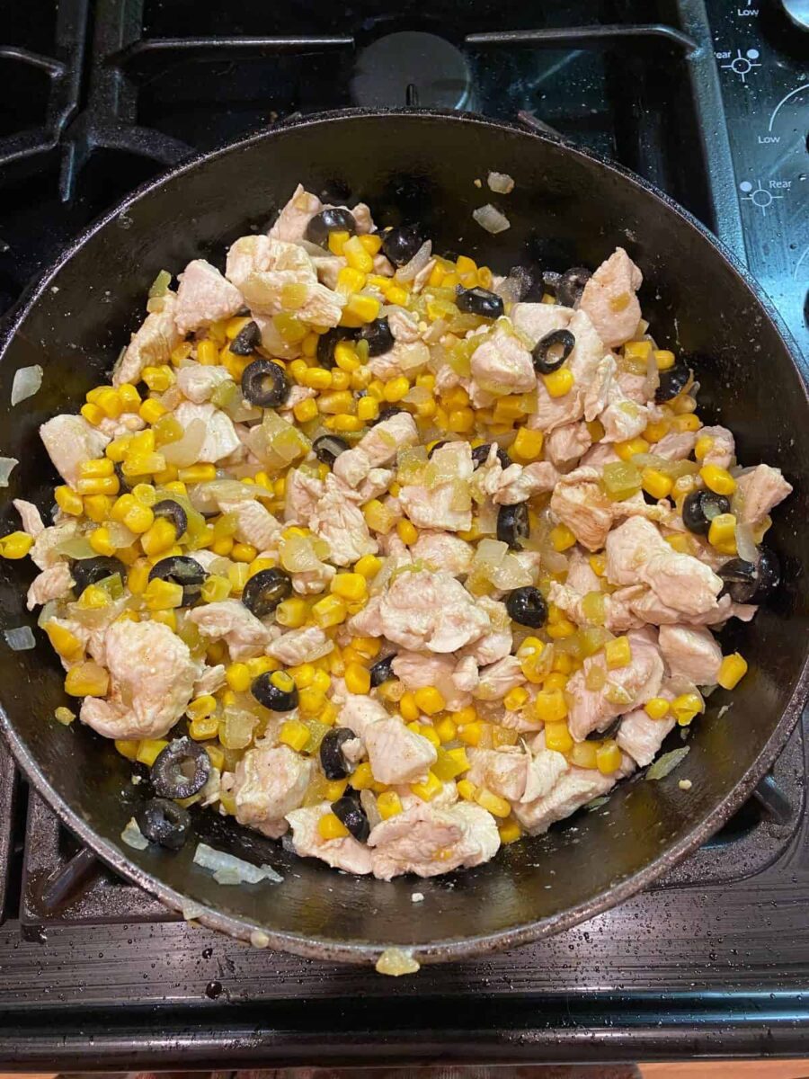 Chicken, olives, corns and seasonings mixed in a cast iron skillet.