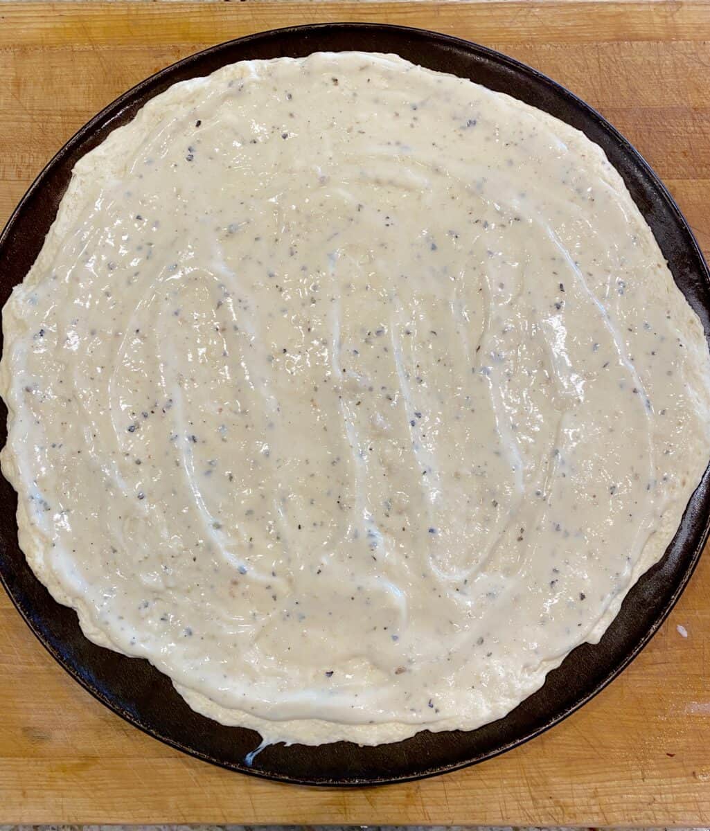 White pizza sauce on a large pizza crust in a pan.