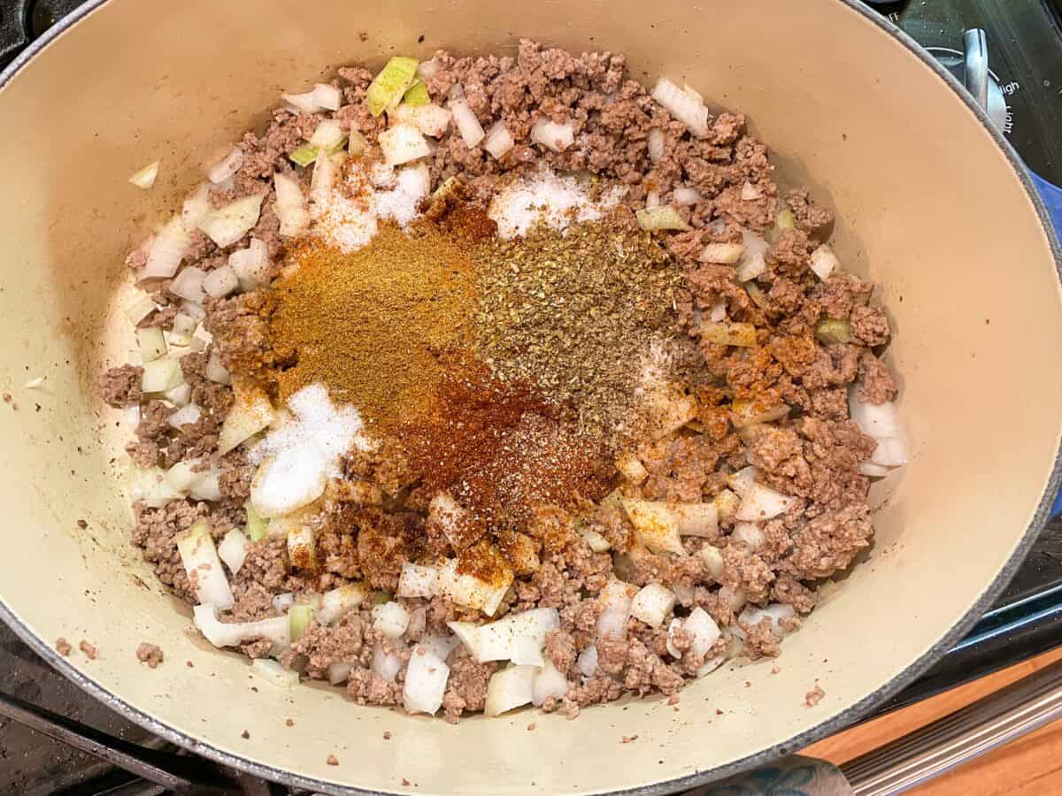 Spice ingredients for Idaho chili placed on top of browned meat and diced onions in a large stockpot.