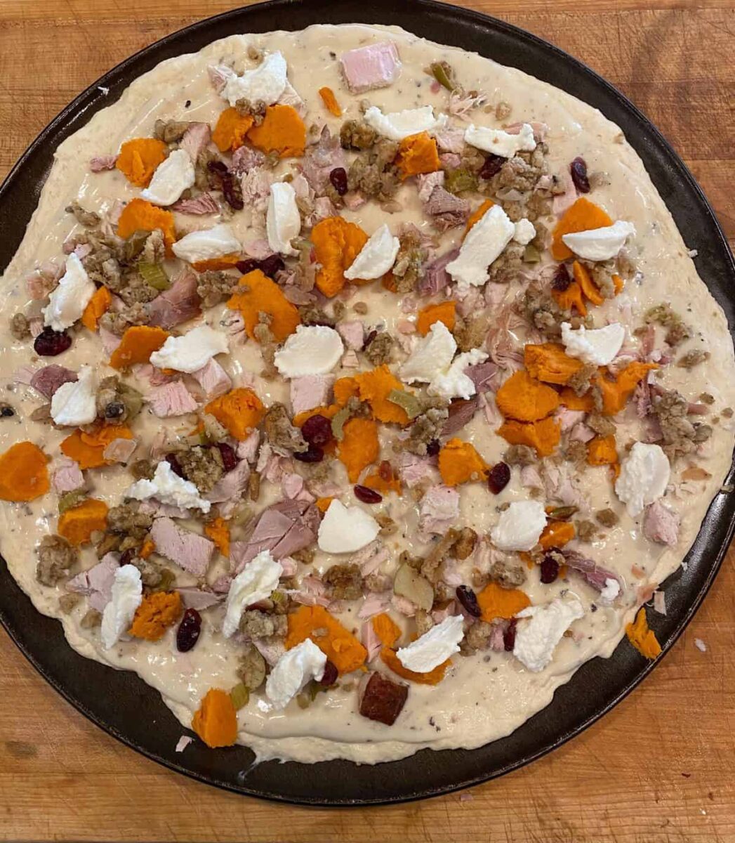 Unbaked leftover turkey pizza on a cutting board.