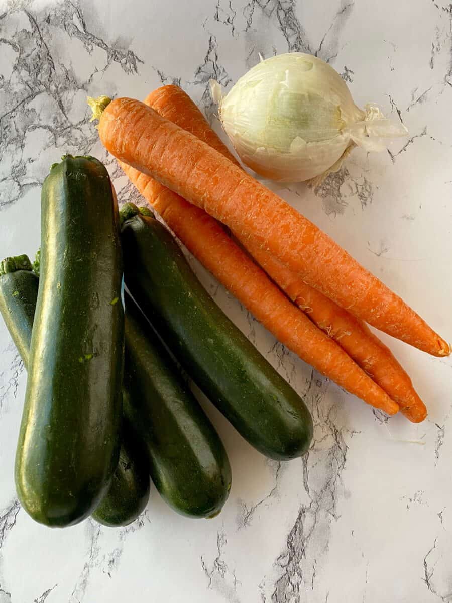 Four zucchinis, three carrots and an onion on a counter.