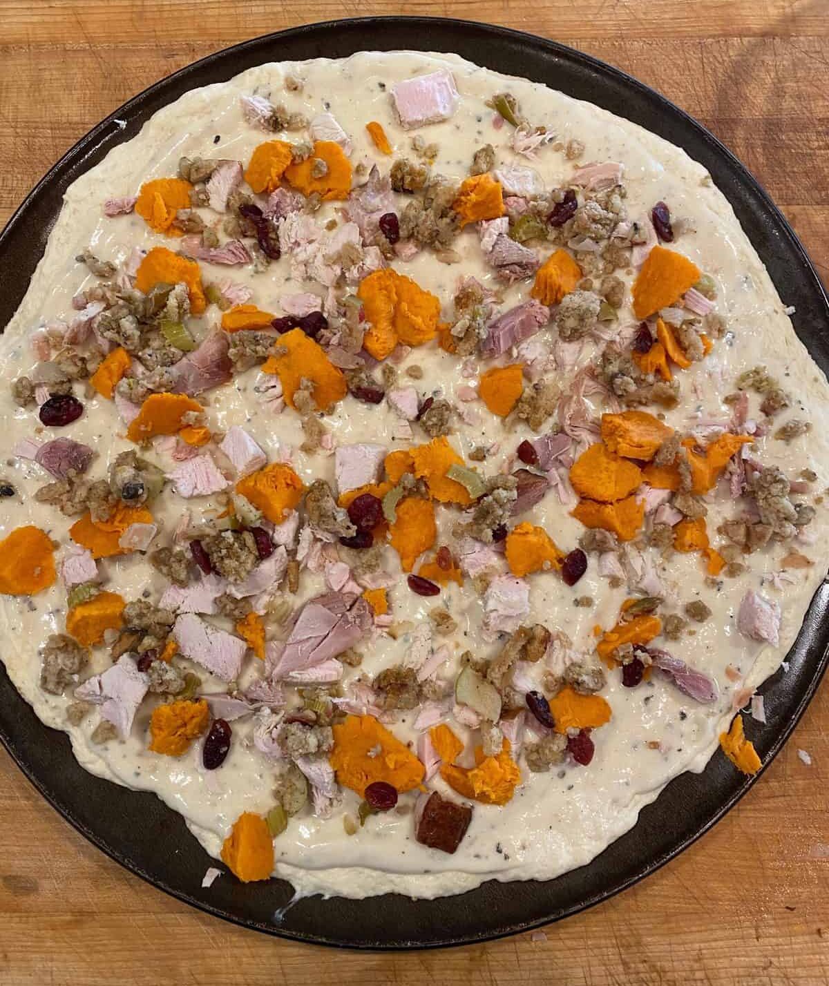 Leftover turkey, sweet potatoes and stuffing spread out on white pizza sauce.