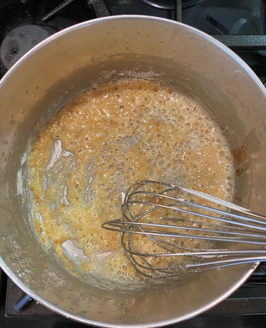 Butter and flour mixed together with a whisk in a pan on the stove.